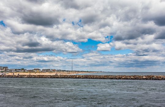 Wide angle photo of the New Jersey Shore. The ocean, inlet, jetty, beach, town, and sky are shown in the New Jersey seaside town of Manasquan.