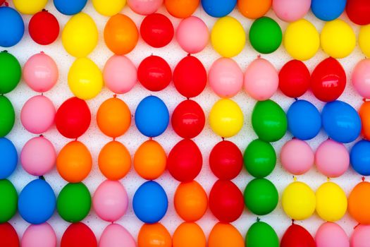 A white wall with colorful balloons attached. Photo is of a boardwalk arcade game where you throw darts and try to pop balloons. Only the wall of balloons is shown.