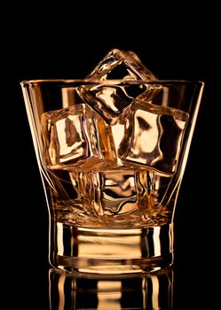 Empty whiskey glass with ice cubes on black background