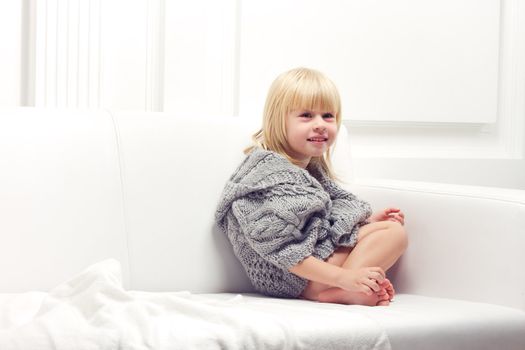 Girl 3 years old in a gray knit sweater sitting on a sofa