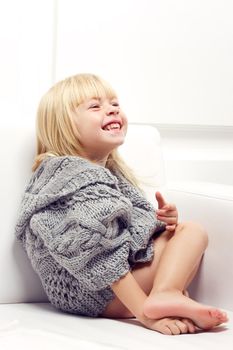 Girl 3 years old in a gray knit sweater sitting on a sofa