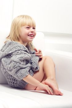 Girl 3 years old in a gray knit sweater sitting on a sofa