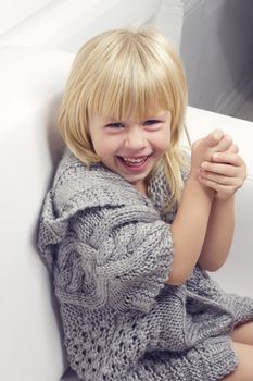 Girl 3 years old in a gray knit sweater sitting on a sofa