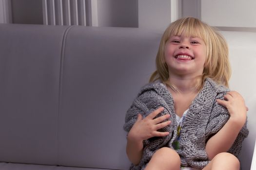 Girl 3 years old in a gray knit sweater sitting on a sofa