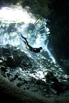 A young woman freedives into a cenote. An underwater cave system in Mexico.