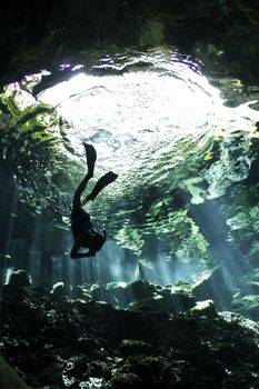 A young woman freedives into a cenote. An underwater cave system in Mexico.