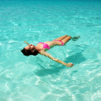 Woman in bikini lying on water at tropical beach