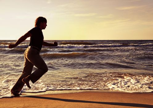 Man running along seashore in summer evening