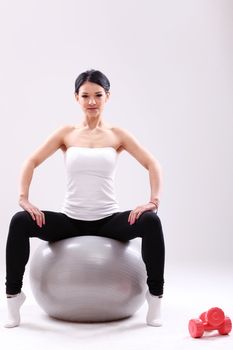 Cute young fitness girl sitting on abs ball in studio