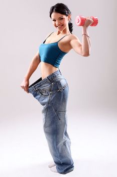 Cute and slim girl with dumbbell wearing old jeans after weight loss