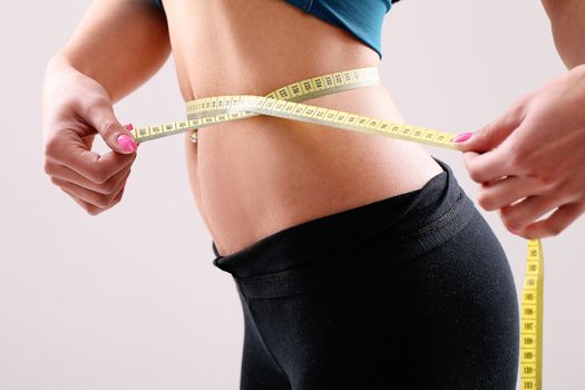 Slim girl measuring her waist with ruler in studio