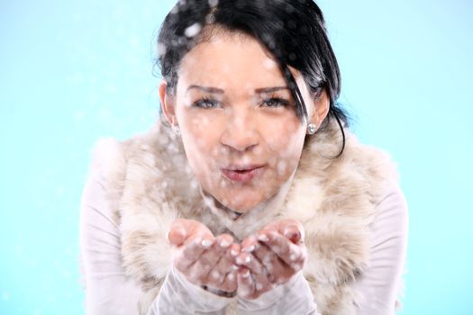 Cute and attractive girl blowing on christmas snow isolated on a blue