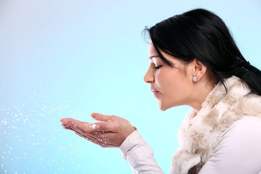 Cute and attractive girl blowing on christmas snow isolated on a blue