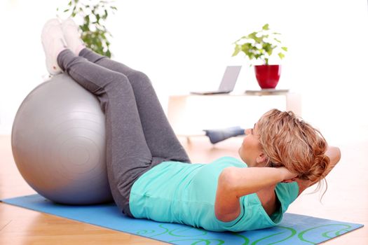 slim mid aged woman do her exercises with abs ball at home