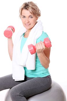 Cute mid aged women with towel do exercises with dumbbells ona a ball