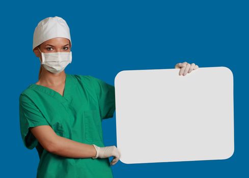 A young woman doctor holding an empty white bill board against a blue background.