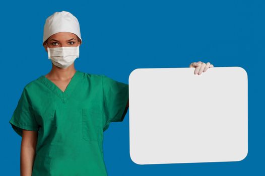 A young woman doctor holding an empty white bill board against a blue background.