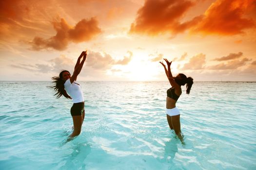 Two happy wimen playing in water on sunset