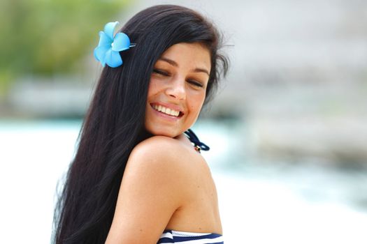 Close-up portrait of young smiling woman with tropical flower in hair