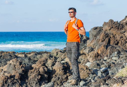 Young man in glasses with backpack. Backround blue sea