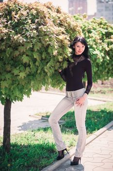 Young woman standing near a maple with lush foliage