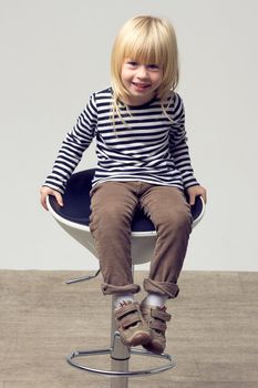 Blonde girl 3 years old in jeans sits on a high chair