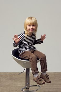 Blonde girl 3 years old in jeans sits on a high chair