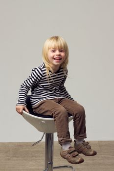Blonde girl 3 years old in jeans sits on a high chair