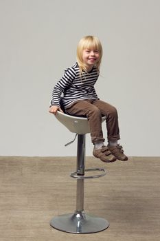 Blonde girl 3 years old in jeans sits on a high chair
