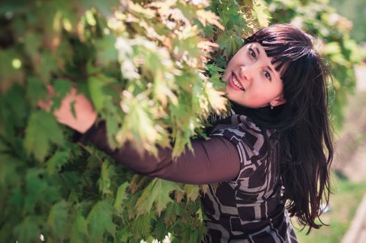 Young woman standing near a maple with lush foliage