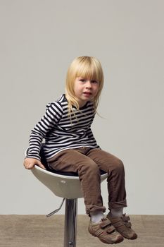 Blonde girl 3 years old in jeans sits on a high chair