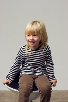 Blonde girl 3 years old in jeans sits on a high chair