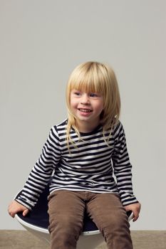 Blonde girl 3 years old in jeans sits on a high chair