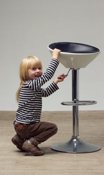 Blonde girl 3 years sat near a high chair and doing something