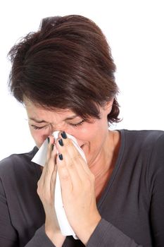 A brunette woman sneezes into a tissue: studio portrait for cold or flu concept Woman suffering from a seasonal winter cold and flu sneezing and blowing her nose on a handkerchief, head and shoulders studio portrait on white