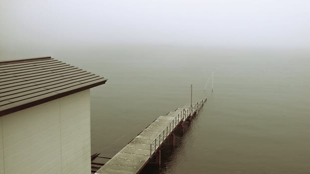 old sinking pier and building on the misty lake shore