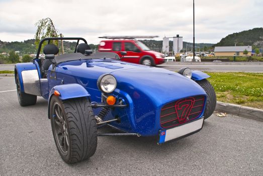 The Caterham 7 (or Caterham Seven) is a super-lightweight sports car produced by Caterham Cars in the United Kingdom. It is based on the Lotus Seven, a lightweight sports car sold in kit and factory-built form by Lotus Cars, from the late 1950s to the early 1970s. The Caterham 7 is a small, lightweight, two-seater sports car renowned for its performance and handling.  Image is shot in Halden city.