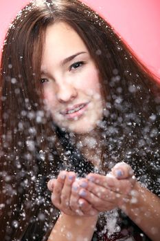 Beautiful and attractive girl blowing on christmas snow isolated on a red