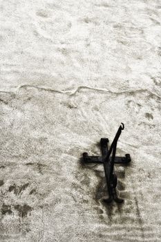 Old rusty metal wall bracket with a hook and a cross shaped base mounted on a grungy rough plastered old wall of a buidling with copyspace