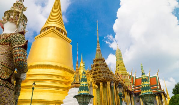 Grand Palace and Wat Phra Kaew Temple interior, Bangkok, Thailand. The Emerald Buddha temple. Visible are one of the many Buddha temple in interior of Grand Palace. Dramatic cloudscape with blue sky and cumulus clouds over the Grand Palace. Specific Thai and Buddha Architecture.