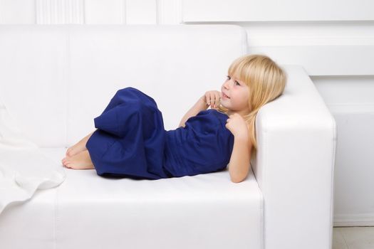 3 years old girl is in a blue dress on a white sofa