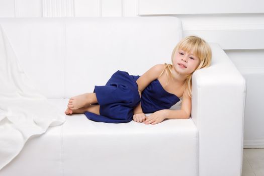 3 years old girl is in a blue dress on a white sofa