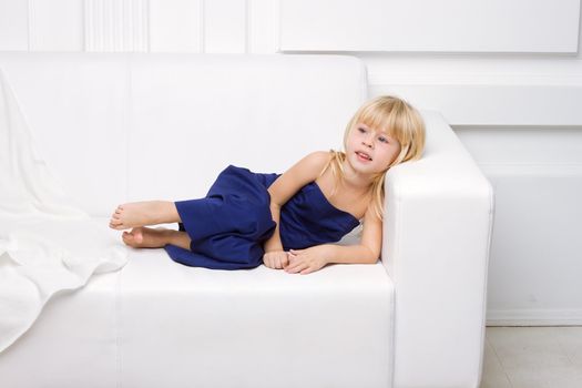 3 years old girl is in a blue dress on a white sofa