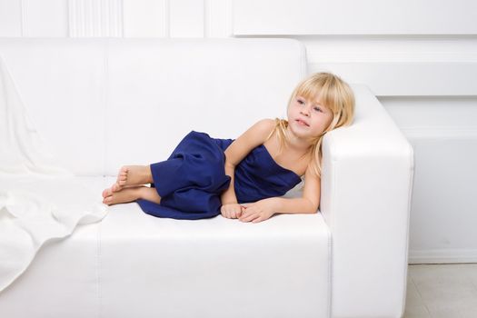 3 years old girl is in a blue dress on a white sofa