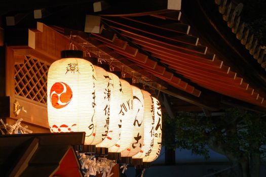 row of traditional Japanese lanterns under the wooden temple roof at Yasaka Shrine in Kyoto, Japan
