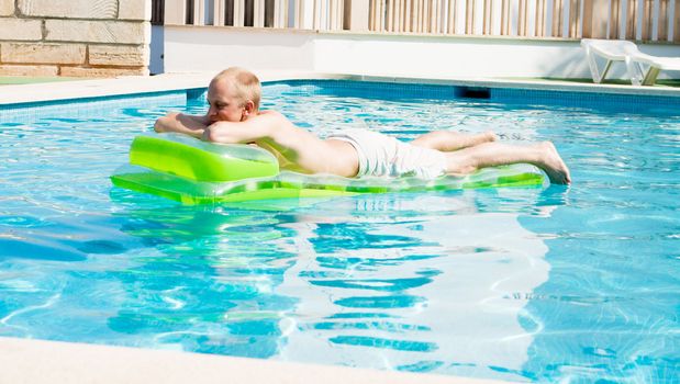 young man is swimming with air mattress in pool in summer vacation