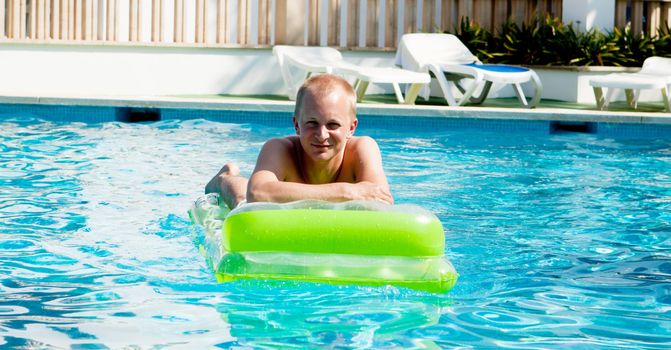 young man is swimming with air mattress in pool in summer vacation