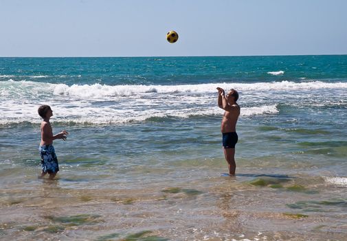 Father and son playing with a ball in the sea .
