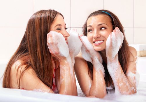 two tricksy beautiful women in jacuzzi with foam on hands