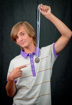 Portrait of a teenager boy   with a medal on a dark background .